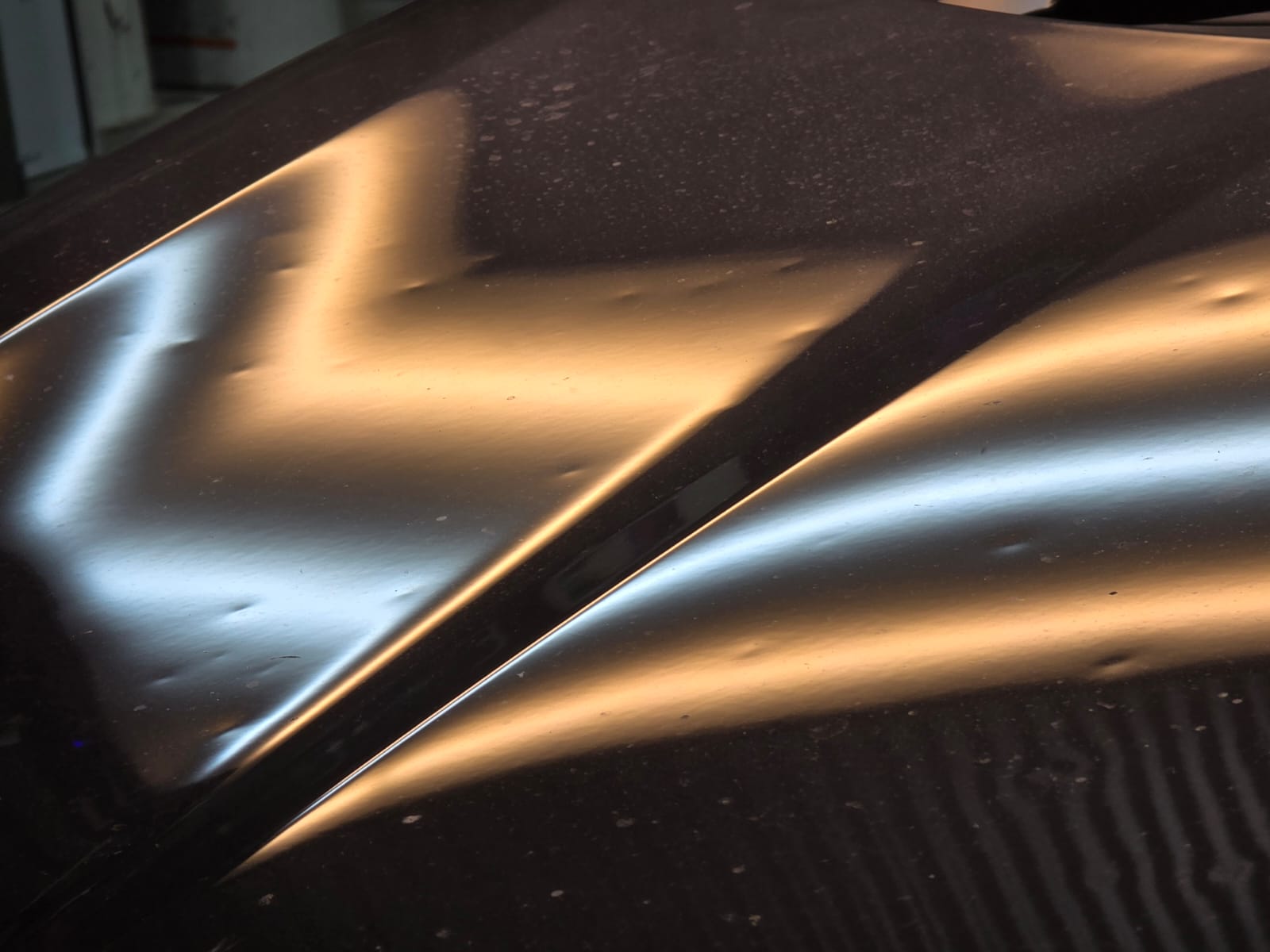 Hail damage on a car roof showing dozens of dents under reflected light